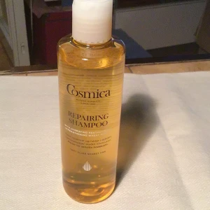 Cosmica Repairing Shampoo 250ml - Cosmica Repairing Shampoo är en genomskinlig, gyllengul flytande schampo i plastflaska med vitt lock. Innehåller panthenol och vetextrakt som återfuktar och stärker håret. Passar för torrt eller skadat hår och är dermatologiskt testad samt vegansk.