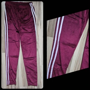 Vinröda sammetstights med vita ränder - Säljer ett par nya , endast provade, softa   vinröda  tights med två vita ränder längs sidorna. Byxorna har resår i midjan och är gjorda i ett mjukt, glansigt material som känns riktigt skönt mot huden. Perfekta för chill eller träning. STRL L