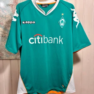 Werder Bremen 2007/08 Kappa home shirt, size XL - Werder Bremen matchtröja från Kappa i storlek XL. Tröjan är grön med vita detaljer, citibank-logga på bröstet och klubbmärke med stjärna. Korta ärmar, vita inslag på sidorna och orange kant nertill. Tillverkad i lätt och ventilerande polyester.