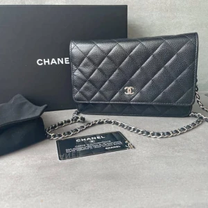 Svart quiltad axelväska från Chanel - Säljer en stilren svart axelväska från Chanel med klassiskt quiltat mönster och silverfärgad kedja. Väskan är tillverkad i skinn och har det ikoniska CC-emblemet framtill. Perfekt storlek för det viktigaste och har en praktisk ficka på baksidan.