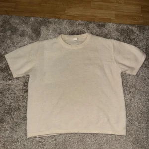 Beige stickad t-shirt från Gina Tricot - Säljer en beige stickad t-shirt från Gina Tricot i storlek 170. Tröjan har rund hals och korta ärmar, perfekt för dig som gillar en enkel och clean look. Materialet är mjukt och skönt stickat, vilket gör den superbekväm att ha på sig.