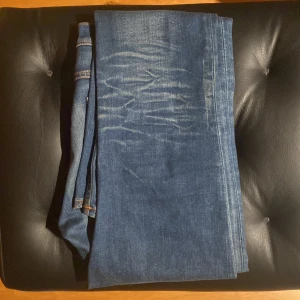 Blå skinny jeans från Nudie Jeans - Snygga blå skinny jeans från Nudie Jeans med klassiska orange sömmar och coola slitningar på framsidan och baksidan. Jeansen har fem fickor, knappgylf och är tillverkade i mjukt denimtyg som sitter tajt längs benen.