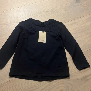Mörkblå blus med spets från Zara Girls - Supersöt mörkblå blus från Zara Girls med långa ärmar och fina spetsdetaljer i form av blommor vid halsringningen. Tillverkad i mjuk bomull och perfekt för dig som gillar en stilren look med en twist.