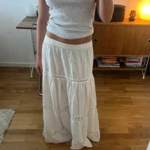 Vit långkjol med spetsdetaljer - Säljer en vit långkjol med bred resår i midjan och flera lager med snygga spetsdetaljer. 