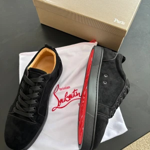 Christian Louboutin svarta sneakers mocka - Svarta sneakers från Christian Louboutin i lyxig mocka med klassisk röd sula. Svarta snören och diskreta metalldetaljer vid snörningen. Insidan är beige och sulan har Louboutins signaturprägling. Perfekt för dig som vill sticka ut med stil.Allt org ingår självklart 