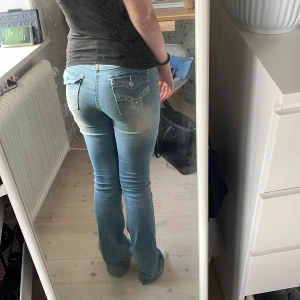 Blå bootcut jeans med dekorerade fickor - Säljer ett par ljusblå bootcut jeans med snygga detaljer på bakfickorna. Jeansen har klassisk femficksdesign och är tillverkade i stretchigt jeansmaterial som sitter skönt. Perfekta för dig som gillar en lite utsvängd look nertill.