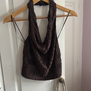 Brun halterneck topp Gina Tricot - Säljer en brun halterneck topp från Gina Tricot i storlek XS. Toppen har en snygg draperad framsida, tunna axelband och struktur i tyget som ger en cool effekt. Perfekt för dig som vill sticka ut med en trendig och unik topp. Användt på klubb🥰