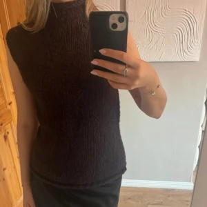 Mörklila stickad väst från Bik Bok - Säljer en bruna stickad väst från Bik Bok med hög krage. Västen har en chunky, grovstickad look och är ärmlös med rak passform. Perfekt att styla över en långärmad tröja för extra lager. Färgen är djup och ger en cool vibe till din outfit.