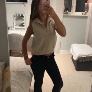 Beige stickad croppad väst med zip - Säljer en beige stickad väst med krage och dragkedja framtill. Modellen är croppad och har en loose passform, perfekt att styla över en t-shirt eller skjorta. Västen har ribbad struktur och är ärmlös för en chill vibe.
