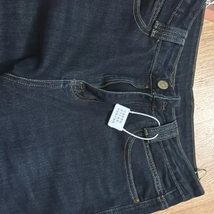 Mörkblå jeans med breda uppvik - Snygga mörkblå jeans från Mini med breda uppvik nertill och dekorativa metallmärken. Klassisk femficksmodell med kontrastsömmar och rak passform. Jeansen har dragkedja och knapp i midjan och är tillverkade i slitstark denim.