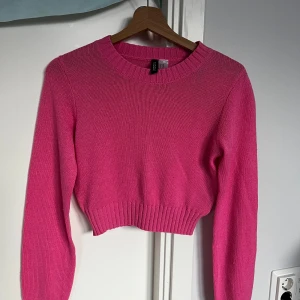Croppad rosa stickad tröja H&M Divided - Superfin croppad stickad tröja i stark rosa från H&M Divided. Tröjan har rund halsringning, långa ärmar och bred ribbad mudd vid ärmslut och nederkant. Perfekt för att liva upp din outfit med en poppig färg!