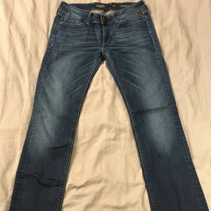 Replay blå jeans med dragkedjor - lågmidjade blå jeans från Replay med  dragkedjor på bakfickorna. Jeansen har kontrastsömmar, Replay-logga i metall och läderdetalj bak. Passformen är lite bootcut och materialet är slitstarkt denim. storlek w26 L34!!!