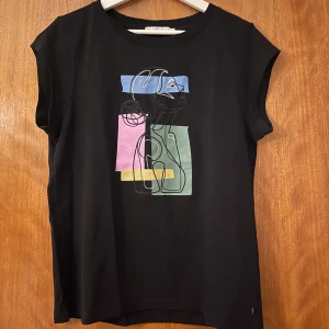 Svart t-shirt med grafiskt tryck - Svart t-shirt från Coster Copenhagen  med korta ärmar och ett  grafiskt tryck i blått, rosa, grönt och gult på bröstet. Skön passform och rund halsringning. 