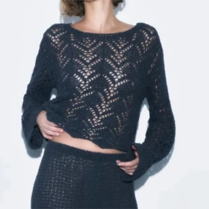 Mörkblå stickad croppad tröja - Snygg mörkblå stickad tröja med genombrutet mönster och croppad passform. Tröjan har långa ärmar och ett coolt hålmönster som ger en trendig look. Perfekt att styla med höga byxor eller kjol.