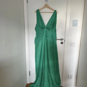 Grön långklänning från Flounce London - Snygg grön långklänning från Flounce London med djup v-ringning och breda axelband. Klänningen har ett subtilt leopardmönster i tyget och är tillverkad i ett glansigt, mjukt material som faller fint. Perfekt för dig som vill sticka ut med en cool och trendig look.