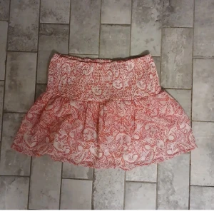 Rosa mönstrad kortkjol från Gina Tricot - Supersöt kortkjol från Gina Tricot i rosa och vitt med ett snyggt mönster. Kjolen har bred smock i midjan och volangig nederdel som ger en luftig känsla. Perfekt för varma dagar och enkel att matcha med en enkel topp.