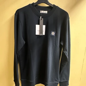 Stone Island sweatshirt, XXL - Snygg mörkblå sweatshirt från Stone Island med rund hals och lång ärm. Tröjan har en stilren design med logopatch på bröstet och ribbade muddar vid ärmslut och nederkant. Perfekt för dig som gillar clean streetwear.