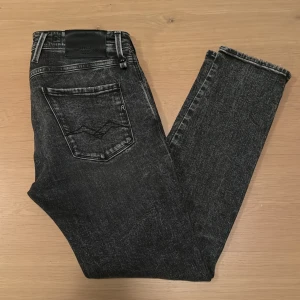 Replay Anbass jeans - Svarta Replay Anbass jeans i slim fit med cool tvättad look och klassiska fem fickor. Tillverkade i ekologisk bomull för extra skön känsla. Snygga kontrastsömmar och detaljer på bakfickan. Perfekta för dig som gillar stilrena och moderna jeans.