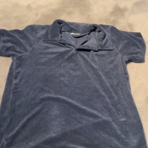 Blå frotté pikétröja med krage - Mjuk och chill blå pikétröja i frotté med klassisk krage och korta ärmar. Perfekt för dig som gillar en avslappnad vibe och vill ha något som sticker ut lite med sin unika textur. Passar lika bra till jeans som till shorts.