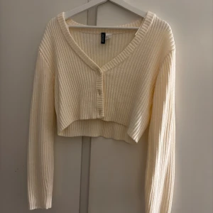 Croppad kofta från H&M  - Superfin croppad kofta i krämvit färg från H&M. Ribbstickad med v-ringning och knappar framtill. Långärmad och i mjukt material som passar att ha över exempelvis ett linne eller så som den är💘