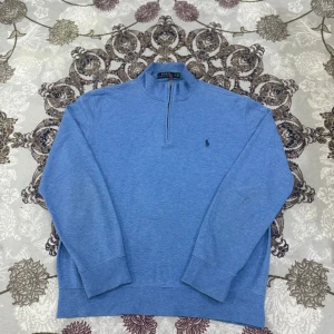 Blå Polo Ralph Lauren half-zip tröja - Klassisk och stilren blå half-zip tröja från Polo Ralph Lauren. Tillverkad i mjukt och bekvämt bomullsmaterial med den ikoniska broderade loggan på bröstet. Perfekt för både vardag och mer avslappnade tillfällen.  Längd från axeln och ner: 62 cm Bredd under armhålorna: 46 cm  📦 Skickas snabbt & välpackat.