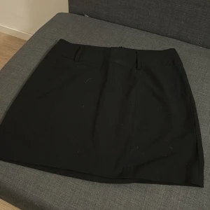 Svart kortkjol från KappAhl - Stilren svart kortkjol från KappAhl med klassisk rak passform och diskret dragkedja bak. Kjolen har bred linning och är gjord i ett mjukt polyestermaterial som känns bekvämt mot huden. Passar bra som M