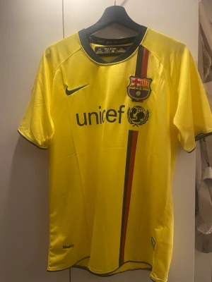 FC Barcelona bortatröja – Ibrahimovic #9 - FC Barcelona bortatröja i gul färg med Zlatan Ibrahimovic på ryggen, nummer 9. Tröjan är i storlek M och har klassiska detaljer som UNICEF-loggan framtill, LFP-märket på ärmen och ”més que un club” på insidan av kragen. Ett riktigt fint plagg för samlare eller Barça-supporters, och ett starkt minne från Zlatans tid i klubben. Tröjan är i nytt skick