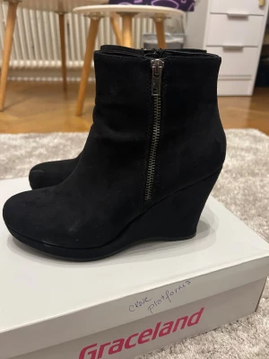 Svarta kilklacksboots från Graceland - Säljer ett par svarta boots från Graceland med kilklack och dragkedja på sidan. Skorna har rund tå och är gjorda i mocka-look som ger en snygg och stilren vibe. Perfekta att styla med jeans eller kjol för en cool look. Boxen medföljer