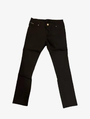 Svarta byxor från Philipp Plein - Svarta byxor från Philipp Plein med raka ben och snygga guldfärgade detaljer på knappar och nitar. Klassisk femficksmodell med diskret logga på fickan. Materialet känns mjukt och stretchigt, perfekt för en clean och stilren look.