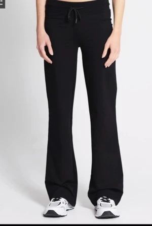 Svarta bootcut mjukisbyxor med snörning - Svarta mjukisbyxor med bootcut-snitt och snörning i midjan. Byxorna har en avslappnad passform och är tillverkade i mjukt material som känns skönt mot huden. Perfekta för chill dagar eller när du vill ha en bekväm stil.