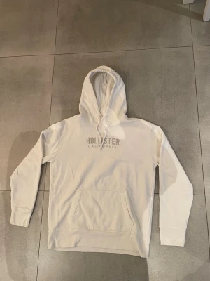 Vit hoodie från Hollister  - Snygg vit hoodie från Hollister, (bland de mest eftertraktade just nu) mycket bra skick med inga defekter, storleken är M och sitter bra på killen som är ca 185. Hör av dig vid minsta lilla, MVH EM_RESELL 