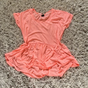 Ljusrosa volangtopp från Gina Tricot - Supersöt ljusrosa topp från Gina Tricot med volang nedtill och korta ärmar. Toppen har en rund halsringning och är tillverkad i mjuk bomull, perfekt för en avslappnad och trendig look. Passformen är loose och modellen är något längre bak.  Den har tyvärr några fläckar lite här och var. Den är stretchig  Färg: ljus rosa Storlek M Från Gina tricot 