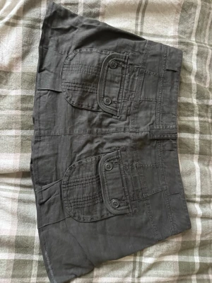 Svart kortkjol från Esprit med fickor - Säljer en svart kortkjol från Esprit i storlek 36. Kjolen har flera stora fickor med knappdetaljer och coola sömmar som ger en avslappnad vibe. Perfekt för dig som gillar praktiska detaljer och en enkel stil. Materialet är mjukt och känns bekvämt mot huden.