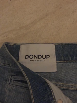 Blå jeans från Dondup george, slim fit - Snygga ljusblå jeans från Dondup, tillverkade i Italien. Modellen har klassisk femficksdesign, smal passform och raka ben. Jeansen är gjorda i mjukt denimtyg med lätt tvättad look och subtila slitningar. Perfekt för dig som gillar stilrena och moderna jeans.