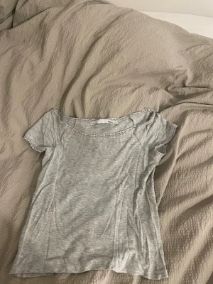 Grå topp med spets från 157 - Säljer en ljusgrå topp från 157 i storlek S. Toppen har korta ärmar och är gjord i mjuk bomull. Runt halsringningen och ärmsluten finns fina spetsdetaljer som ger en söt touch. Perfekt att matcha med jeans eller kjol.