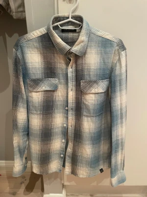 Blåvit rutig skjorta Shine Original - Snygg blåvit rutig skjorta från Shine Original med klassisk krage och två bröstfickor med knappar. Skjortan har långa ärmar och är tillverkad i mjuk bomull, perfekt för en chill och avslappnad stil. Knäppning framtill och coolt mönster som sticker ut.✅Storlek M✅Inga defekter✅