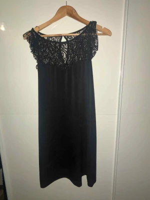 Svart klänning med spetsdetalj - Säljer en svart klänning med vacker spets upptill och rund hals. Klänningen har en rak och enkel siluett, är ärmlös och faller strax ovanför knäna. Perfekt för dig som gillar stilrena plagg med en twist av spets.