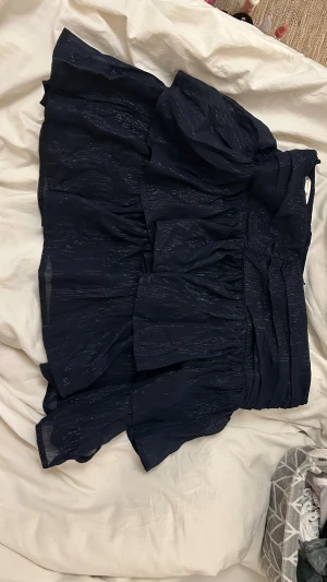 Mörkblå volangkjol - Säljer denna helt oanvända jättefina mörkblå volangkjolen med lite glittriga detaljer från Gina Tricot. Kjolen är i storlek 158/164 men sitter lite lite stort i midjan och är lite för lång för mig (är ca 155cm lång) så skulle säga att den är som en storlek S ungefär men osäker. På bilderna kan man se hur den sitter på när jag har vikt ner midjan. Skriv gärna vid funderingar eller om exakta  mått för kjolen💘