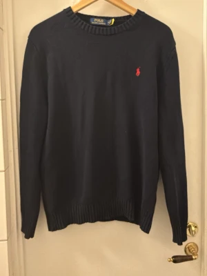 Ralph Lauren mörkblå tröja - Snygg mörkblå stickad tröja från Polo Ralph Lauren med klassisk röd broderad logga på bröstet. Tröjan är i bra skick utan några defekter eller missfärgningar. Den är fantastisk skön att ha nu på vintern och passar till allt! Hör av er vid intresse🏌️💸