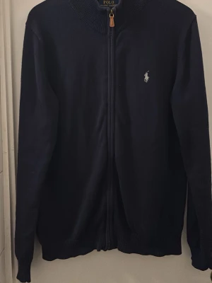 Ralph Lauren zip mörkblå - Snygg mörkblå zip från Polo Ralph Lauren med dragkedja och ribbad krage. Perfekt för alla sammanhang med en grym passform. Kvaliten är 9/10. Hör av er vid intresse!