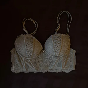 Ljusgrå/ljusgrön spets bh - Säljer en ljusgrå/ljusgrön bh med vacker spets och dekorativ snörning framtill. Bh:n har justerbara axelband, vadderade kupor och fina spetsdetaljer längs nederkanten🍀Använd fåtal gånger!!