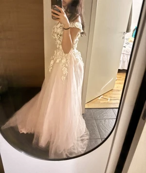 Ljusrosa balklänning med spetsdetaljer - (Klicka på bilden för större bild)Drömmig ljusrosa balklänning med offshoulder och v-ringad överdel. Klänningen har ett lager av tunn tyll och är dekorerad med vita blommiga spetsapplikationer upptill. Kjolen är voluminös och svepande, perfekt för bal eller student. 🩷🩷