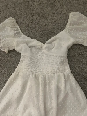 Vit kortklänning med puffärmar - Supersöt vit body, ser ut som en klänning men är shorts i. Med transparenta puffärmar och små prickar i tyget. ”Klänningen” har  v-ringning och lätt volang vid ärmslut. Perfekt för sommarens alla tillfällen och ger en romantisk vibe.