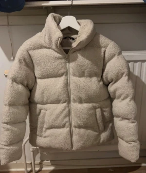 Beige teddy pufferjacka från McKinley - Säljer en beige teddy pufferjacka från McKinley med hög krage och två stora fickor framtill. Jackan har fluffig, quiltad design och stängs med dragkedja. Materialet är polyester och ger en riktigt mysig vibe. Perfekt för kalla dagar när du vill vara både varm och snygg.