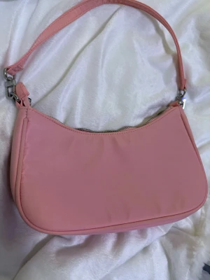 Rosa axelväska från Bik Bok - Snygg rosa axelväska från Bik Bok med stilren design och silverfärgad dragkedja. Väskan har ett huvudfack och en innerficka med dragkedja. Perfekt storlek för det viktigaste och enkel att matcha med olika outfits.