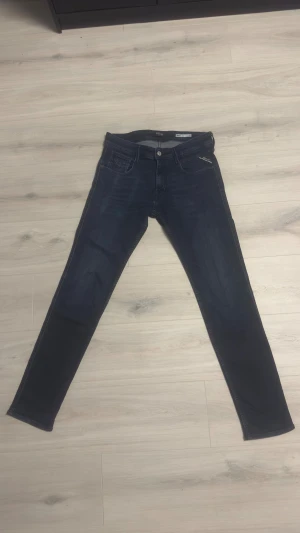 Replay Anbass mörkblå jeans slim fit - Snygga mörkblå jeans från Replay i modellen slim fit. Klassisk femficksdesign med dragkedja och knapp framtill. Jeansen har raka ben och är tillverkade i stretchigt bomullsmaterial för extra komfort. Perfekta för dig som gillar stilrena och moderna jeans.
