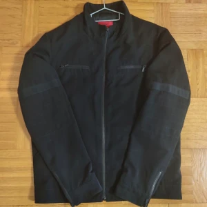 Hugo Boss Jacka - Svart Hugo Boss jacka i storlek XL till salu. Jackan har elegant textur på ärmarna och en liten Hugo logga nedtill. Jackan är i nyskick, inga brister. PRIS KAN DISKUTERAS!