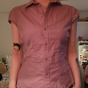 Lila prickig skjorta med kort ärm - Lila skjorta med små prickar och korta ärmar. Skjortan har klassisk krage och knappar hela vägen framtill..