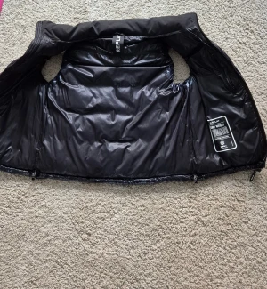 Replay väst - En stilren och funktionell svart och mörkblå  dunväst från Replay, designad för att ge maximal värme och komfort. Västen har en blank, quiltad utsida och en lätt glansig finish som ger ett modernt och exklusivt utseende. Använd bara ett fåtal gånger. Storlek M. Skriv för fler bilder om något otydligt. Pris kan diskuteras