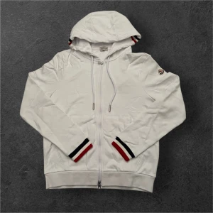 Vit Moncler Zip Hoodie Storlek L (Passar Bättre Som Medium) - Säljer en helt ny vit Moncler hoodie/kofta med dragkedja i storlek L, men den passar bättre en storlek Large enligt mig. Aldrig använd, taggarna sitter fortfarande på.  Stilren och lyxig design med klassisk Moncler-känsla. Perfekt för lager-på-lager nu i höst och vinter.  ✔️ Helt ny, aldrig använd ✔️ Vit färg, dragkedja, huva och Moncler-logga